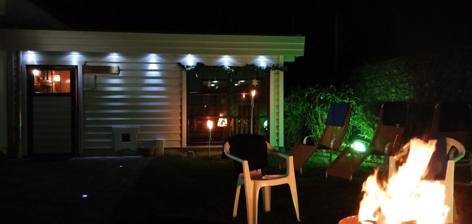 Saunagarten bei Nacht mit Beleuchtung und offenem Feuer