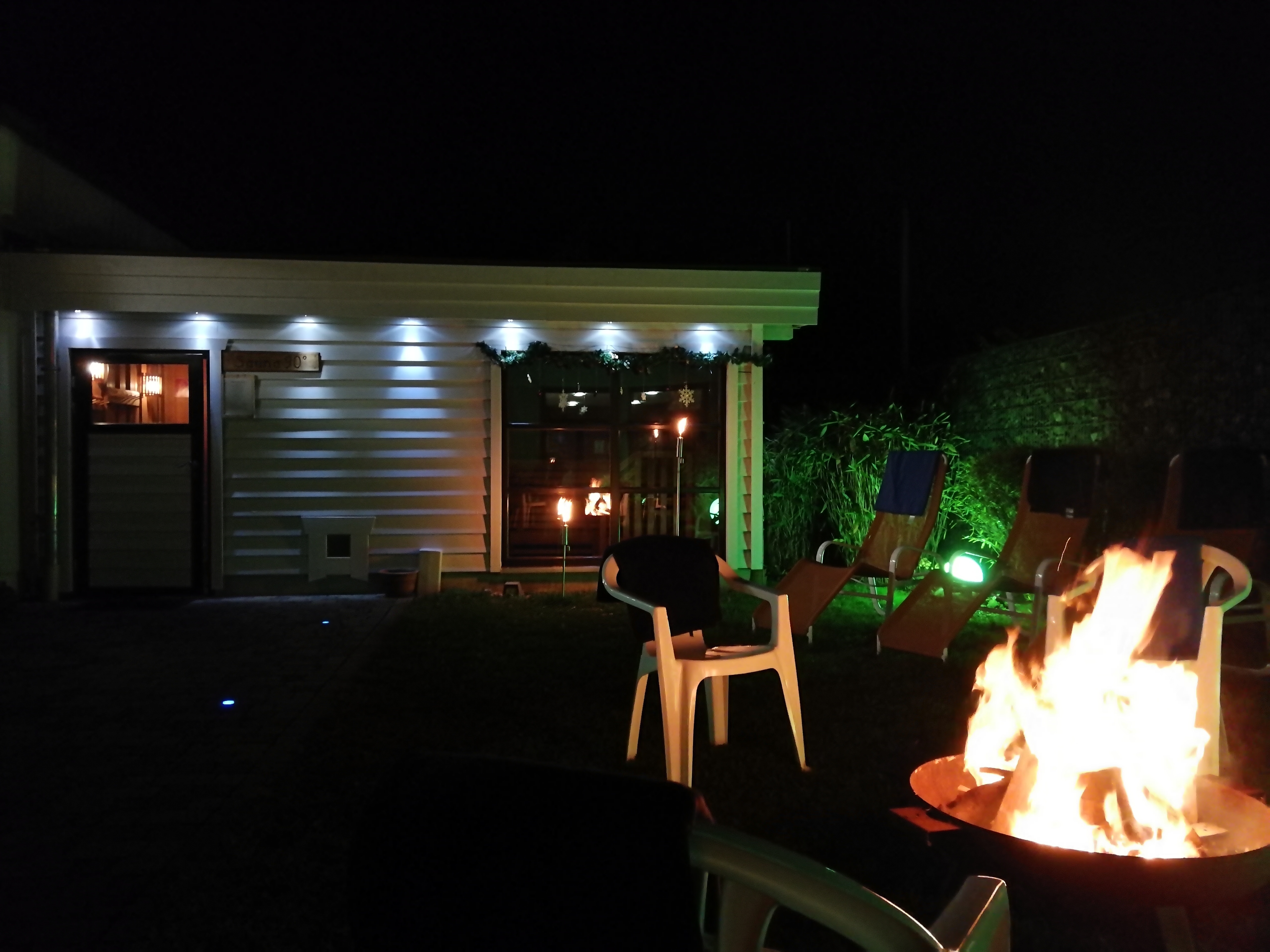 Saunagarten bei Nacht mit Beleuchtung und offenem Feuer