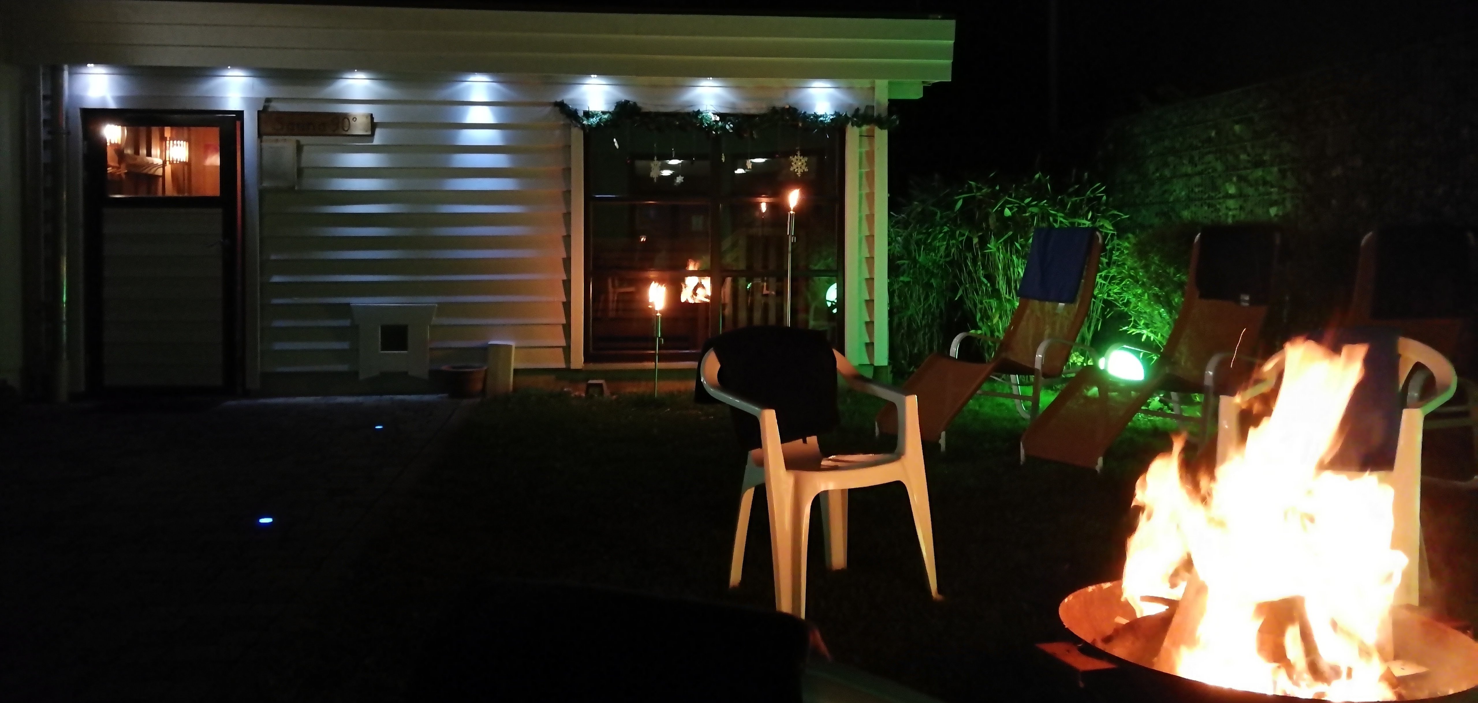 Saunagarten bei Nacht mit offenem Feuer in einer Tonne